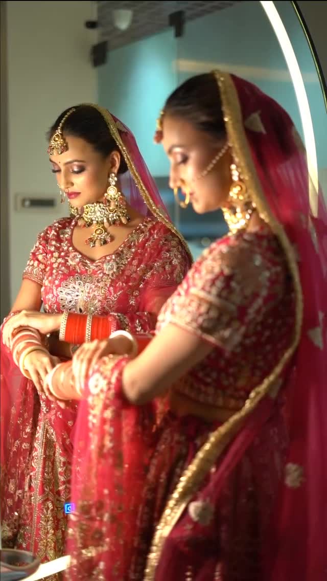Bride in a red bridal lehenga and kundan jewellery admiring her look in the mirror, makeup by Fashion World Palampur